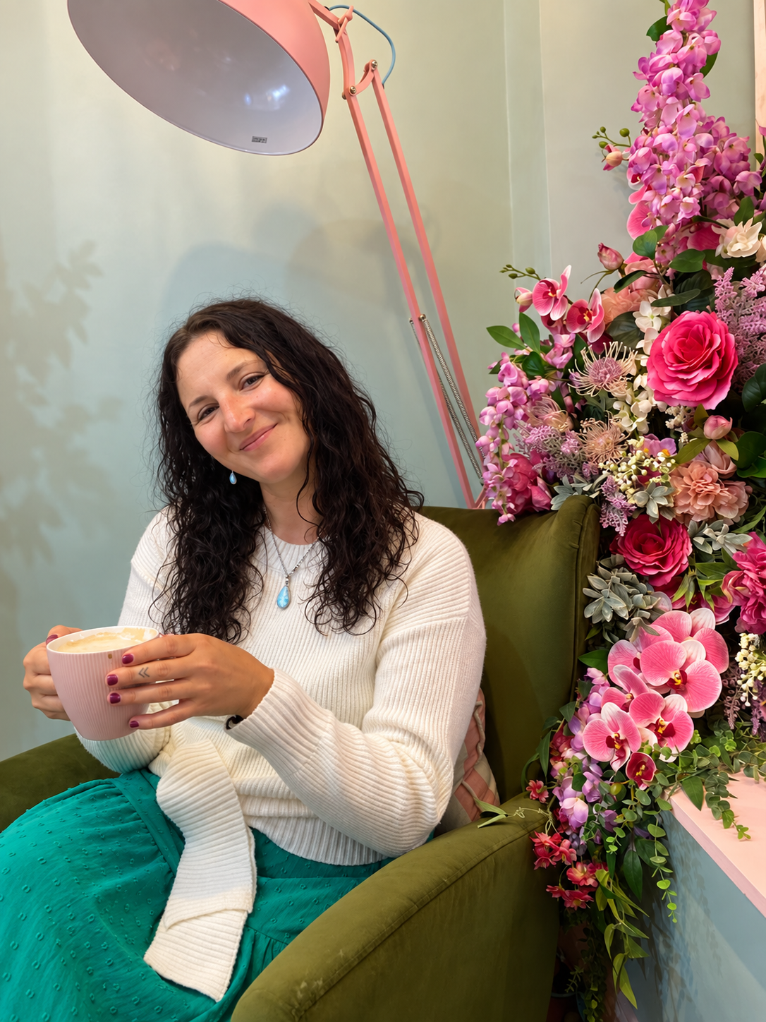 Traci sitting with a warm drink beside a vibrant arrangement of flowers