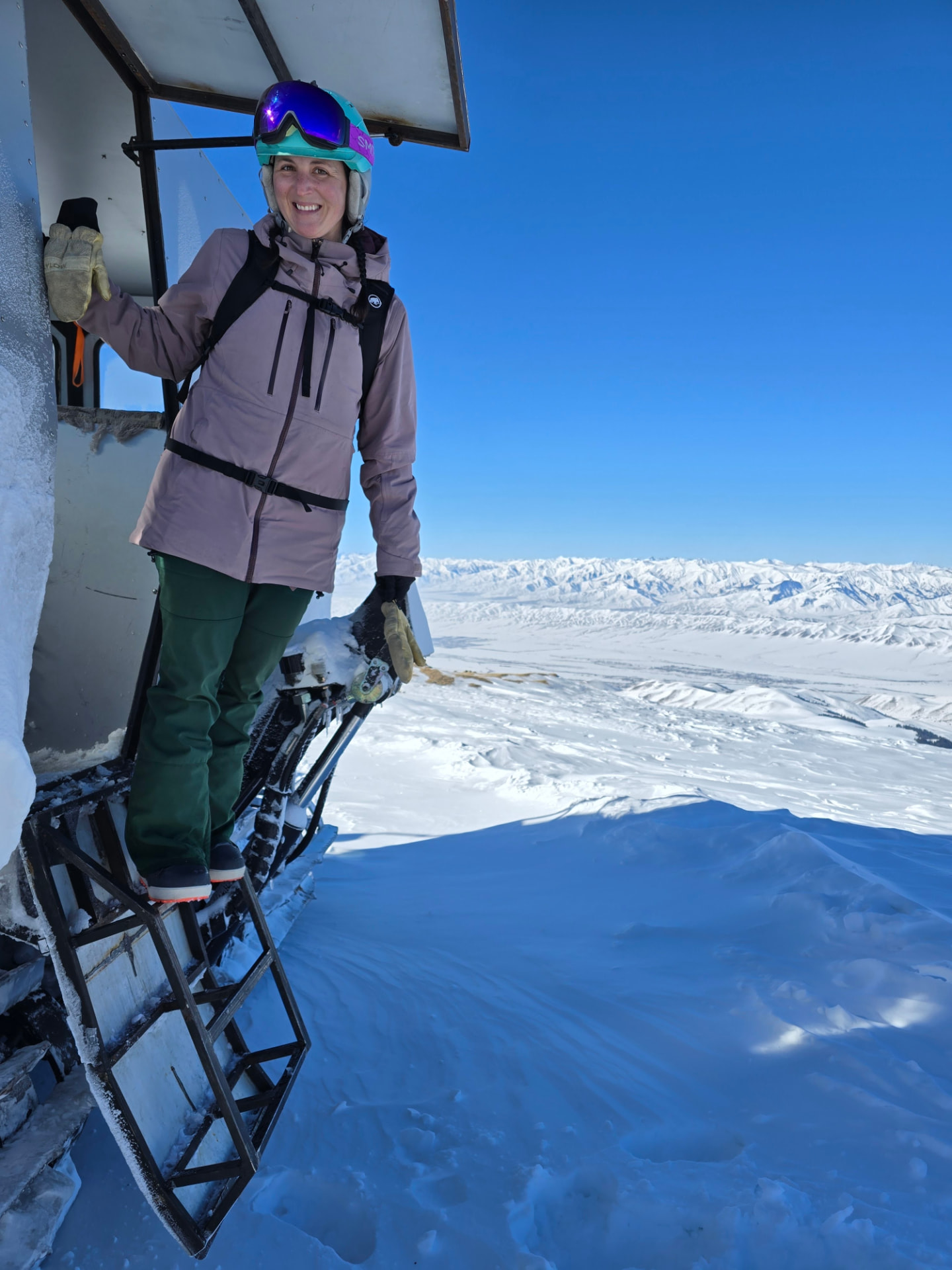 Traci smiling on a snowy mountain above a wide alpine landscape